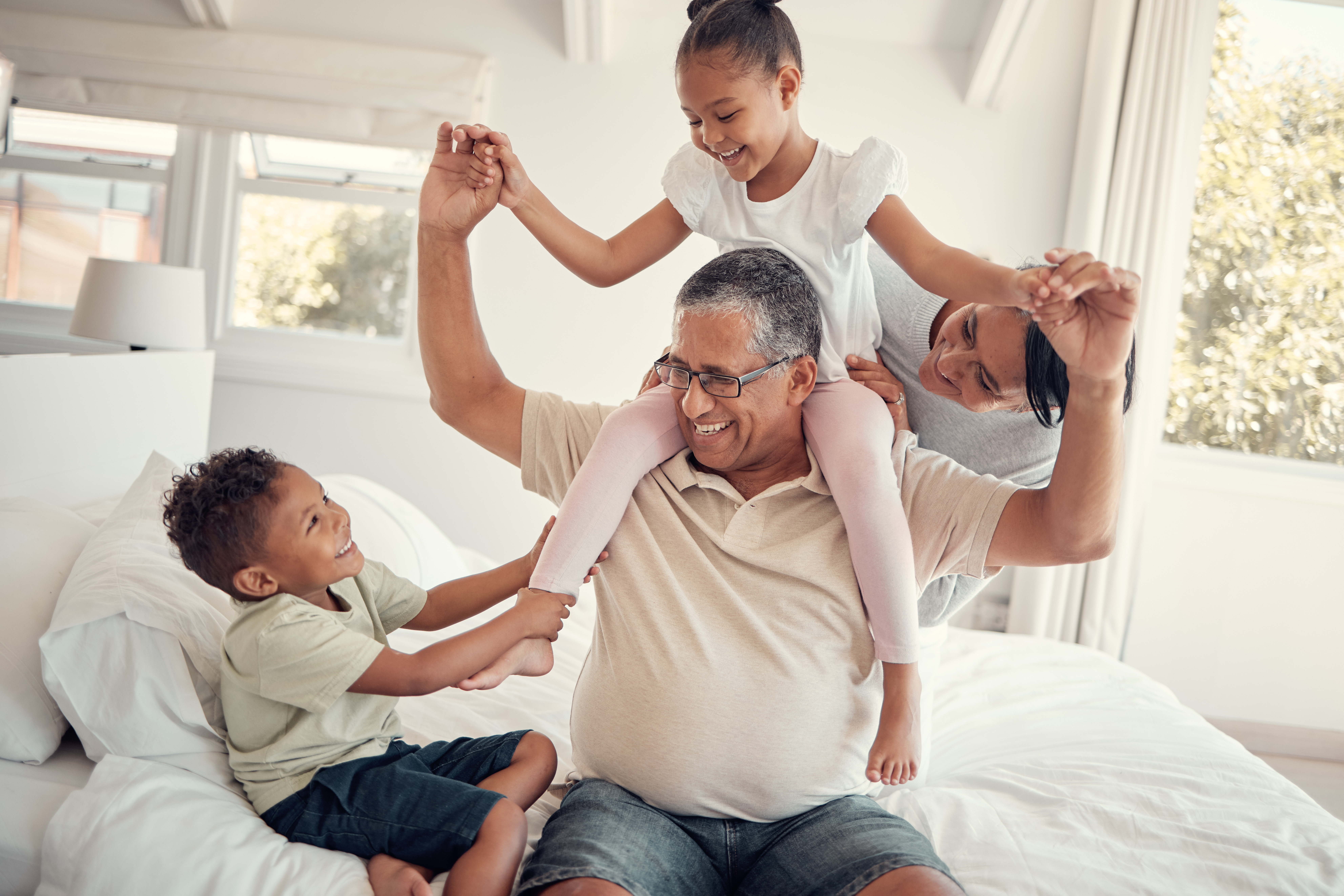 Family, grandfather and piggy back on bed, having fun and bonding. Support, love and care of grandpa, mom and kids playing, enjoying quality time together and relaxing in house on weekend in bedroom